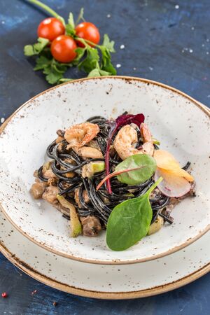Black spaghetti with prawns and mussels seafood pasta on white plate on blue background side viewの写真素材