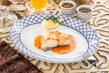 Fried white fish with chili pepper sauce on oriental wooden table side viewの写真素材