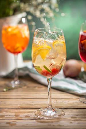Fresh lemonade cocktail with orange, cherry and ice in wine glass splash on wooden table side viewの写真素材