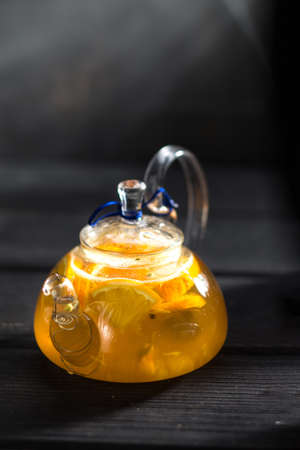 fresh tea with citrus in transparent teapot on a black wooden background side viewの写真素材
