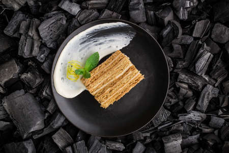 Honey cake slice with cream on black plate on charcoal black background top viewの写真素材