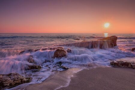 Sea sunrise. Beach and rocks with slow shutter and waves flowing out.の写真素材