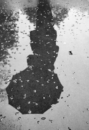reflection of a woman with an umbrella on wet pavement during rain. Black and white. Vertical viewの写真素材