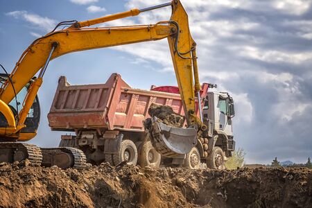 Yellow excavator and empty dump truck working at the construction site