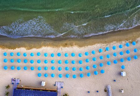 Aerial top view of a beautiful small beach with blue umbrellas, and sea waves.の写真素材