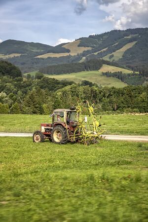 Agricultural machinery, a tractor collecting grass in a field against a blue sky. Season harvesting, grass, agricultural land. Selective focusの写真素材