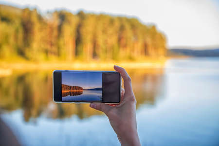 Woman hand holding smartphone taking photo picture of beautiful nature / mobile phone photography and video conceptの写真素材