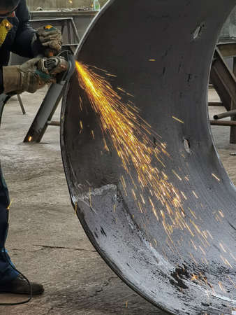 Fly bright sparks from the angle grinder machine. A young male welder in gloves grinds a metal...