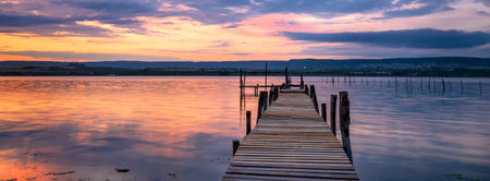Amazing mood sunset at a lake coast with a boat at a wooden pier. Panoramic viewの写真素材