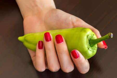 Beautiful female hand with a red nails holding green pepper.の写真素材