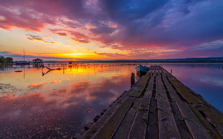 Amazing mood sunset at a lake coast with a boat at a wooden pierの写真素材