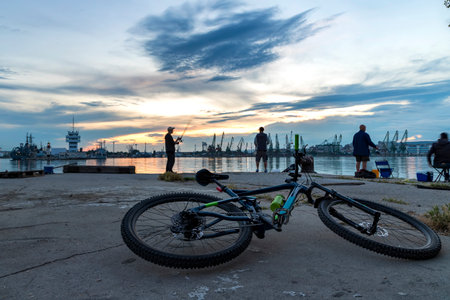A bicycle on the shore and silhouettes of fishermen at a beautiful sunsetの写真素材