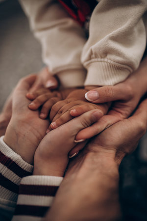 Close-up of Three hands clasped together, child and adult, wearing white sweater and striped sleeves. Soft focus, neutral background. Concept of family, unity, and connection.の写真素材