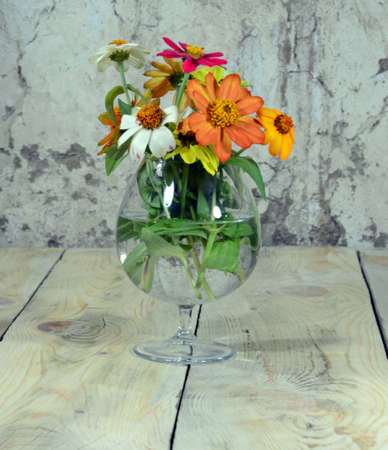 A bouquet of beautiful flowers is placed in a beautiful glass cup filled with water, which is placed on a table made of worn wood.の写真素材