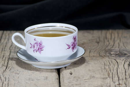 The tea in a beautiful white floral tea cup is placed on an old wooden tableの写真素材
