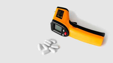 Electronic thermometer on a white background next to pills.