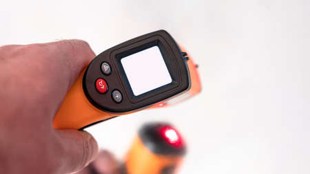 Electronic thermometer in hand with white screen.