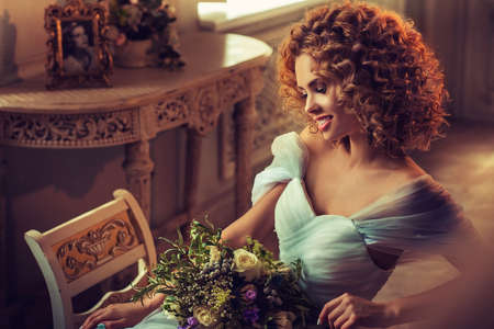 Nice smiling young girl model with dense, curly hair, dressed in evening gown and big earings. Portrait in classical interior.の写真素材