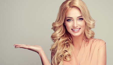 Attractive blonde woman with wide smile and  points to the side and presents your product.の写真素材