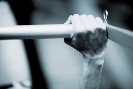 Hand of a young woman realising an exercise of pilates on a pilates machine bar in a healthclub gym specialized training room. Black and white monochrome photo in blue tone.の写真素材