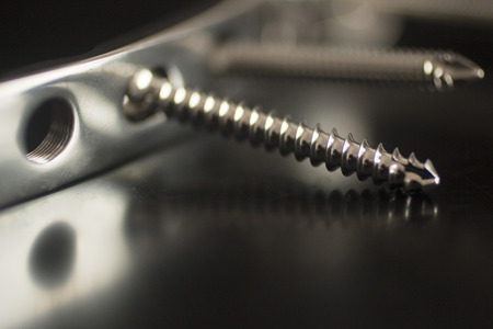Traumatology orthopedic surgery implant titanium plate and silver color screws in semi silhouette against plain black studio background. Close-up macro horizontal photograph in grey tones with reflection.の写真素材