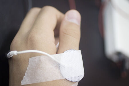 Close-up color horizontal photo in grey tones of a the hand of a young man in medical physiotherapy rehabiliation from injury and traumatology operation surgery with electrical stimulus wire attached with plaster with shallow depth of focus.の写真素材