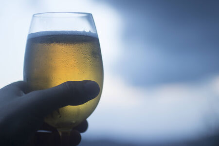 Hand of man holding glass of lager beer set against blue grey sky.Artistic color digital photo with shallow depth of focus.の写真素材