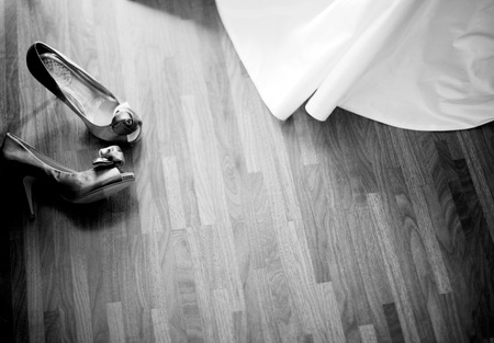 Black and white artistic digital rectangular horizontal photo wedding white dress and bridal shoes of bride on wooden floor of hotel suite bedroom before marriage ceremony. Shallow depth of focus with background defocusedの写真素材