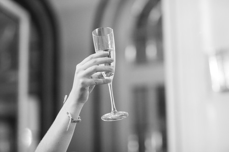 Black and white artistic digital rectangular horizontal photo of hand of young woman in wedding banquet marriage party holding sparkling white wine champagne flute glass in Madrid Spain. Shallow depth of with background out of focus.の写真素材