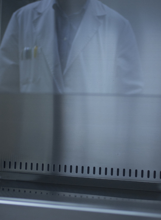 Reflection in laboratory of male lab technician in labcoat and blue shirt with pens in lapel pocket vertical color photo.の写真素材