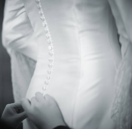 Bride gets help dressing white wedding dress black and white photo.