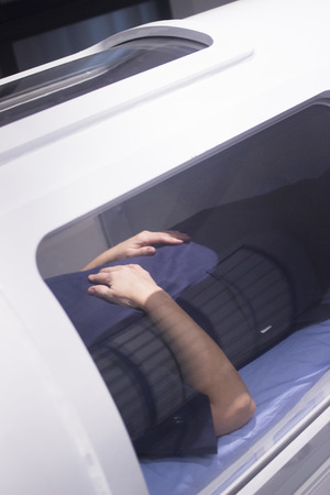 Female patient aged 45-55 wearing flower dress lying down in hyperbaric oxygen chamber receiving...