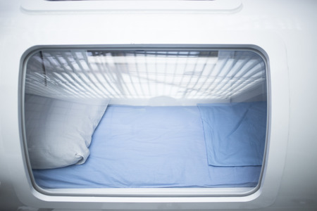 Hyperbaric Oxygen Therapy (HBOT) chamber tank used for specialised medical treatment for injuries in hospital clinic. Exterior viewing window with pillow and bed inside.の写真素材