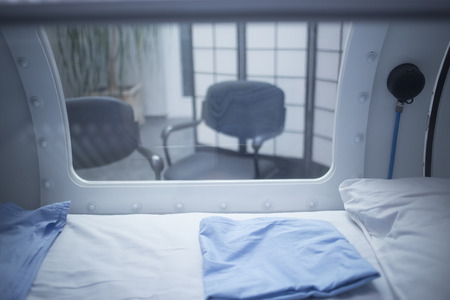 Hyperbaric Oxygen Therapy (HBOT) chamber tank used for specialised medical treatment for injuries in hospital clinic. Exterior viewing window and reflection with pillow and bed inside.の写真素材