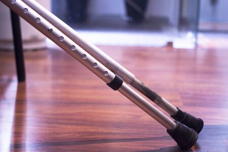 Aluminium metal crutches on floor in hospital clinic waiting room with legs defocused behind.の写真素材