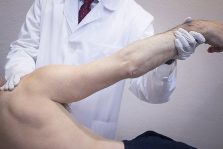 Male Traumatologist orthopedics surgeon doctor examining middle aged man patient to determine injury, pain, mobility and to diagnose medical treatment in shoulder, arm, elbow and wrist.の写真素材
