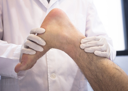 Male Traumatologist orthopedics surgeon doctor examining middle aged man patient to determine injury, pain, mobility and to diagnose medical treatment for foot, ankle, leg and calf.の写真素材