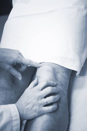 Traumatologist orthopedic surgeon doctor examining middle aged man patient to determine injury, pain, mobility and to diagnose medical treatment in leg, knee meniscus cartilage, ankle and foot injury.の写真素材