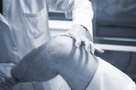 Traumatologist orthopedic surgeon doctor examining middle aged man patient to determine injury, pain, mobility and to diagnose medical treatment in leg, knee meniscus cartilage, ankle and foot injury.の写真素材