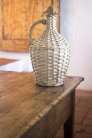 Vintage wine bottle basket on table in old country house.の写真素材