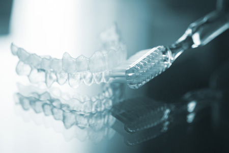 Invisible dental teeth brackets tooth aligners plastic braces retainers to straighten teeth and toothbrush dental hygien care. Orthodontic temporary removable straighteners in dental office dentists surgery clinic.Artistic color photo in creative blue tonの写真素材