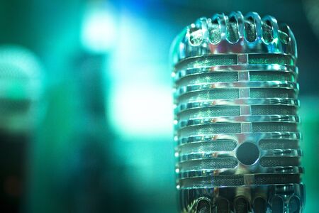 Professional retro vintage large diaphragm studio voice recording concert singing microphone showing metallic body. Artistic color digital photo with shallow depth of focus and negative space and blurred background.の写真素材