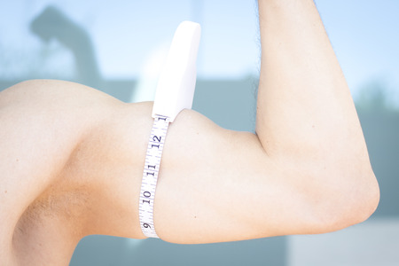Slim attractive young man using measuring tape to measure weight loss o upper arm bicep and tricep.の写真素材