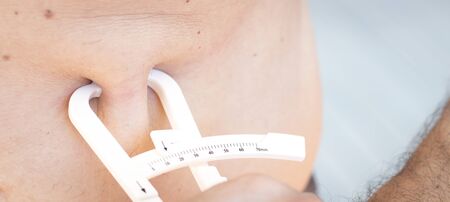 Slim attractive young man using fat caliper to measure bodyfat on waist line.の写真素材