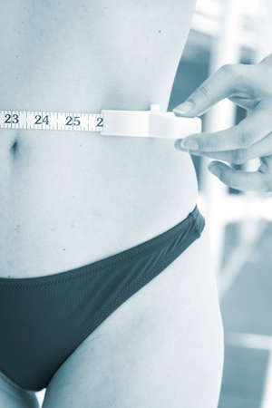 Slim attractive young lady wearing bikini in summer measuring waist with tape to measure waistline during diet.の写真素材