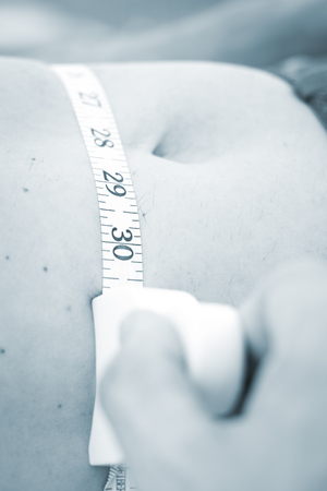 Slim attractive young man using measuring tape to measure weight loss on waist.の写真素材