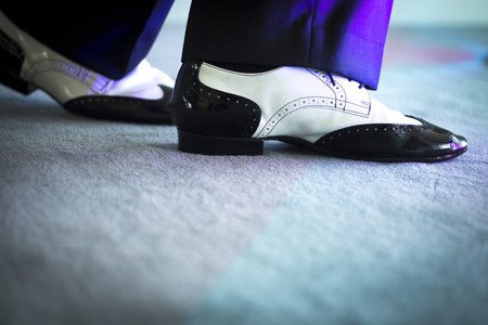 Male latin and salsa dancer in black and white jazz dancing shoes in light and dark on stage.