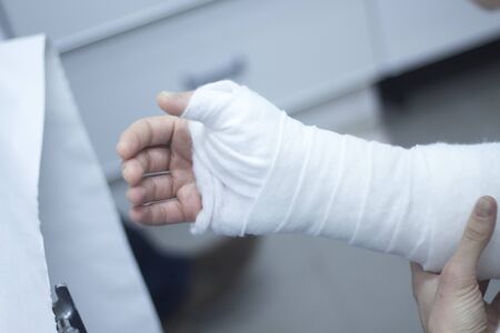 Doctor applying a plaster cast and bandages to patient forearm and wrist to immobilize after fracture injury.の写真素材