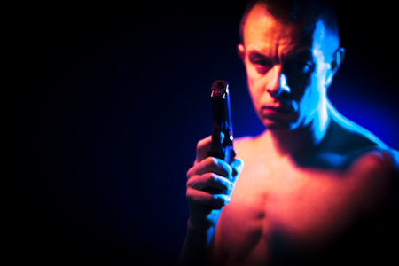 Man in dark with pistol gun nude looking menacing and scary like a killer or assassinの写真素材