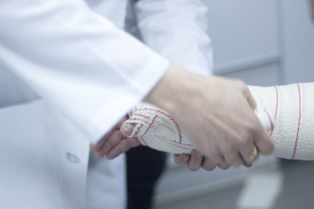 Doctor applying a plaster cast and bandages to patient forearm and wrist to immobilize after fracture injury.の写真素材